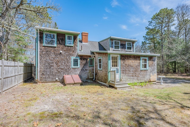 rear view of property featuring roof with shingles, fence, and a chimney