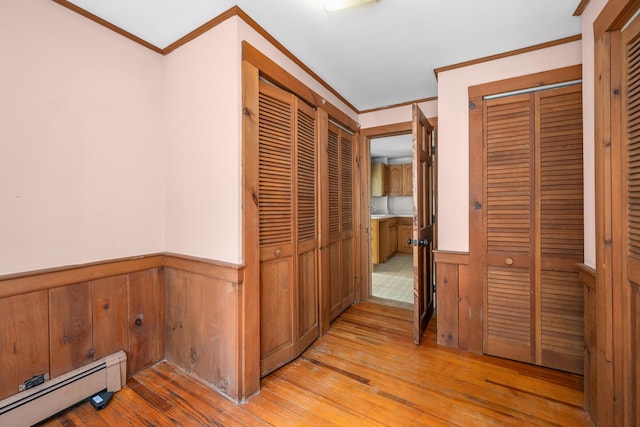 corridor featuring ornamental molding, light wood-style flooring, wainscoting, and baseboard heating
