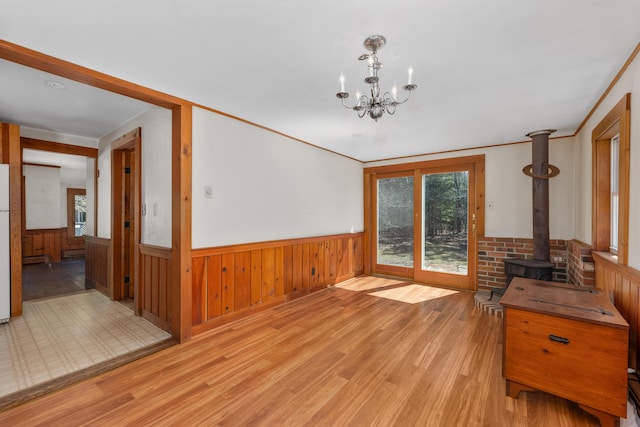 unfurnished dining area with a chandelier, a wood stove, wainscoting, and light wood-type flooring