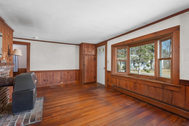 unfurnished living room featuring a baseboard radiator, wood finished floors, wood walls, and a wainscoted wall