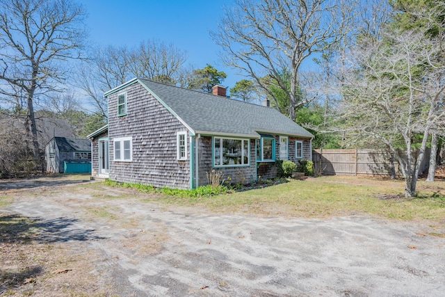 exterior space featuring fence, a chimney, a shingled roof, and a lawn