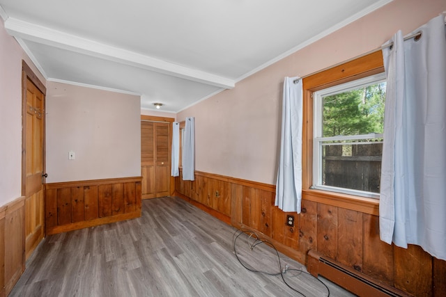 empty room with wooden walls, crown molding, wood finished floors, a wainscoted wall, and a baseboard heating unit