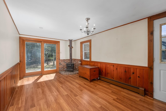 unfurnished dining area with a notable chandelier, baseboard heating, a wood stove, wainscoting, and light wood finished floors