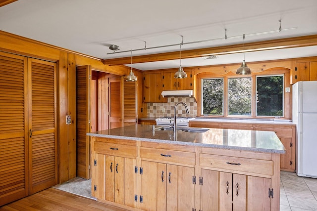 kitchen with white refrigerator, a kitchen island with sink, pendant lighting, and backsplash