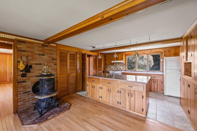 kitchen featuring pendant lighting, white refrigerator, light hardwood / wood-style floors, a wood stove, and sink