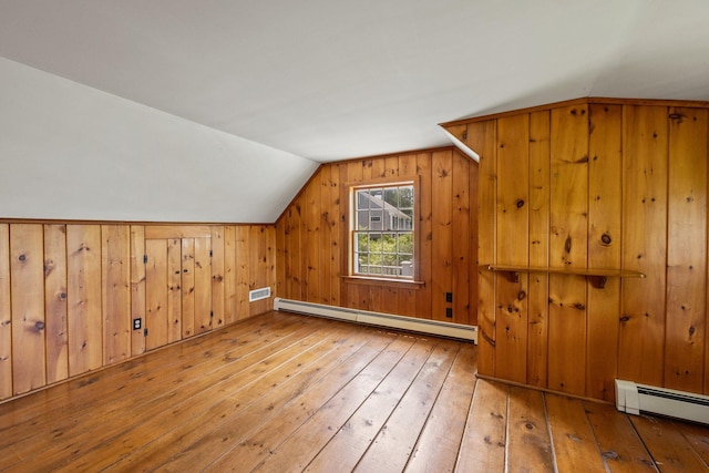 additional living space with light wood-type flooring, vaulted ceiling, wooden walls, and baseboard heating