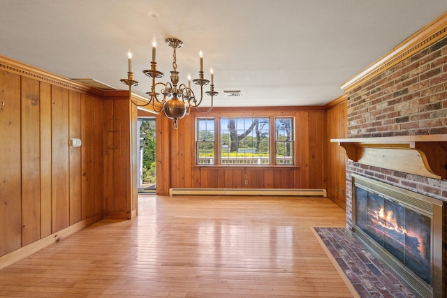 unfurnished living room with a brick fireplace, wooden walls, baseboard heating, and an inviting chandelier