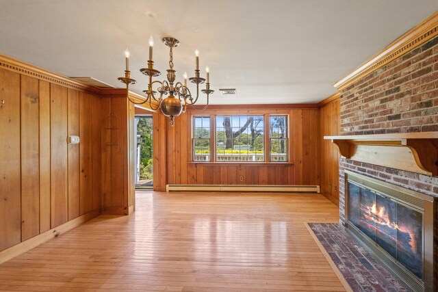 unfurnished living room with a brick fireplace, wooden walls, baseboard heating, and an inviting chandelier