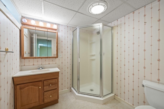 bathroom featuring vanity, toilet, a shower with door, and a drop ceiling