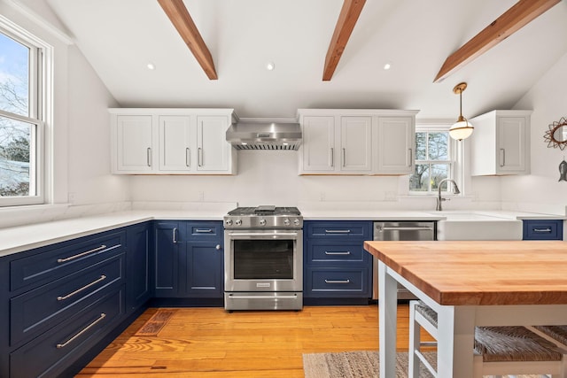 kitchen featuring blue cabinetry, appliances with stainless steel finishes, vaulted ceiling with beams, white cabinets, and wall chimney exhaust hood