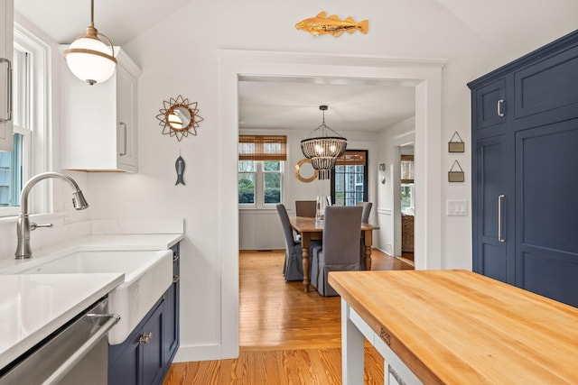 kitchen with pendant lighting, blue cabinets, sink, stainless steel dishwasher, and light wood-type flooring