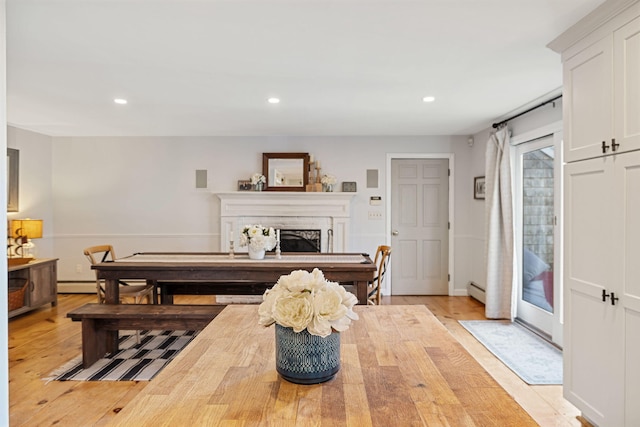 dining area featuring light wood finished floors, recessed lighting, a fireplace, and a baseboard radiator