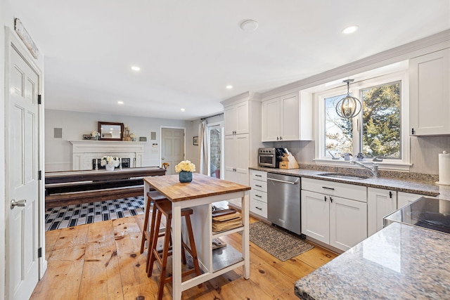 kitchen with stainless steel dishwasher, a fireplace, white cabinetry, and a sink