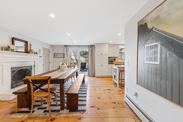 dining space with recessed lighting, light wood-type flooring, a brick fireplace, and a baseboard heating unit