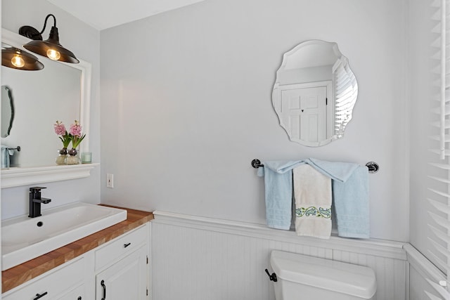 half bath with vanity, toilet, and a wainscoted wall