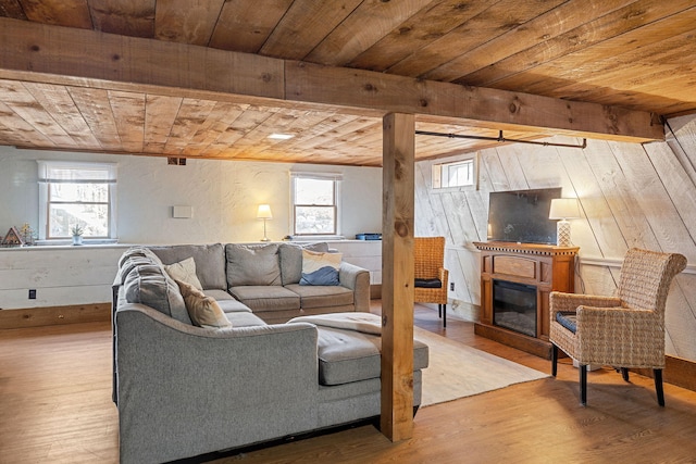 living room featuring a glass covered fireplace, wood finished floors, beam ceiling, and wooden ceiling