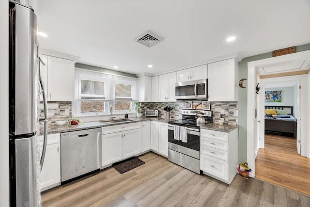 kitchen featuring visible vents, light wood-style flooring, a sink, appliances with stainless steel finishes, and stone counters