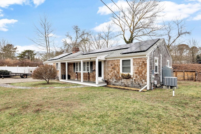 view of front of home with fence, solar panels, covered porch, a chimney, and a front lawn