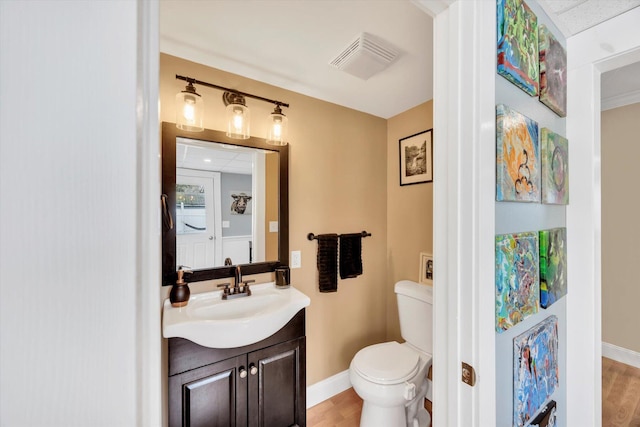 half bathroom with visible vents, baseboards, toilet, wood finished floors, and vanity
