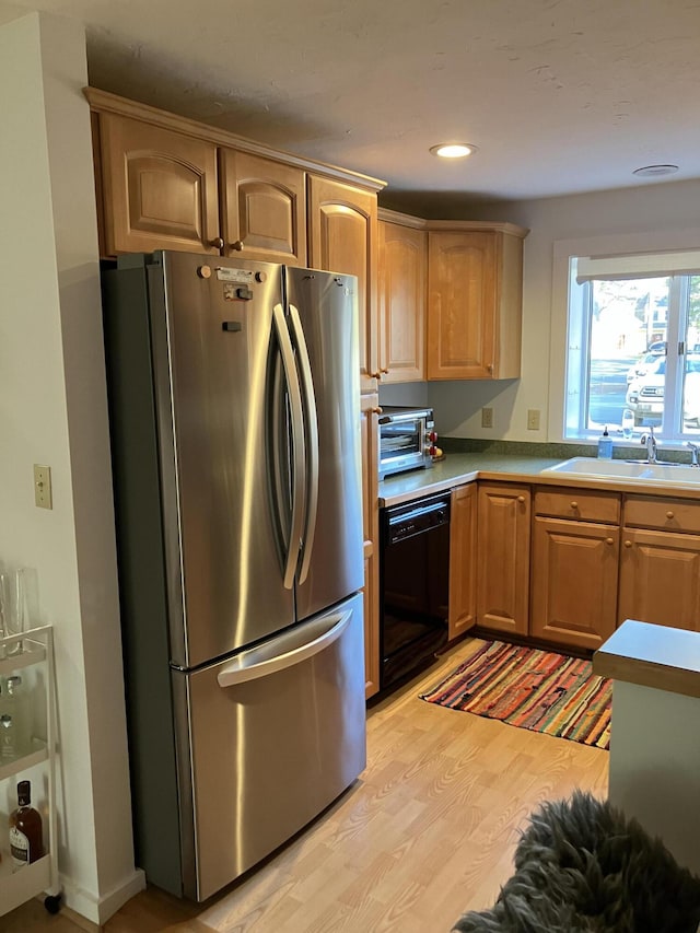 kitchen featuring black dishwasher, sink, stainless steel fridge, and light hardwood / wood-style flooring