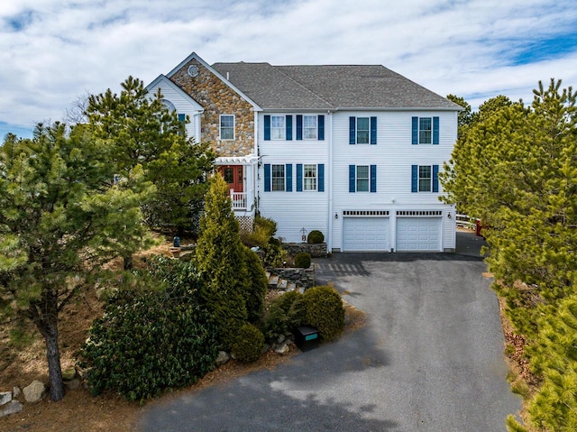 view of front of home featuring an attached garage, stone siding, driveway, and roof with shingles