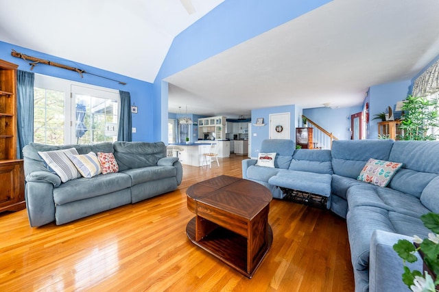 living room with stairs, vaulted ceiling, light wood finished floors, and a chandelier