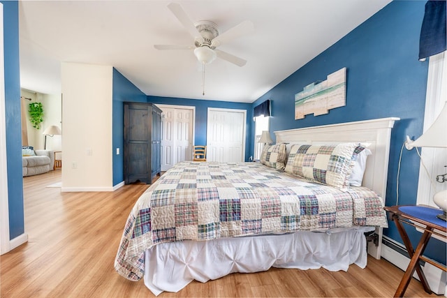 bedroom with a baseboard radiator, baseboards, multiple closets, and wood finished floors