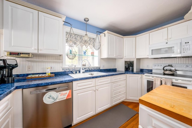 kitchen with white appliances, wood finished floors, a sink, white cabinets, and butcher block counters