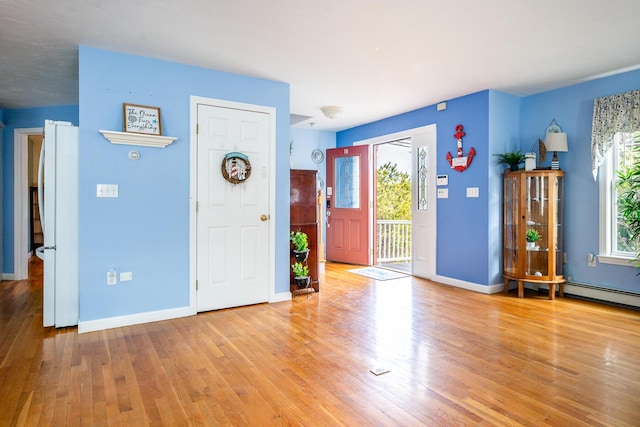 foyer entrance featuring baseboard heating, light wood-style flooring, baseboards, and a healthy amount of sunlight