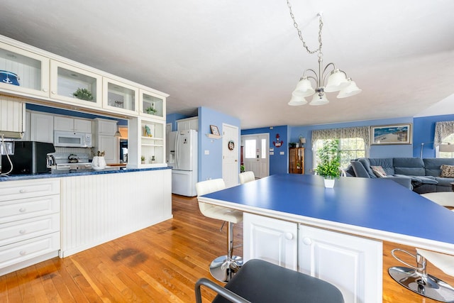 kitchen featuring light wood-type flooring, a breakfast bar, white appliances, white cabinets, and glass insert cabinets