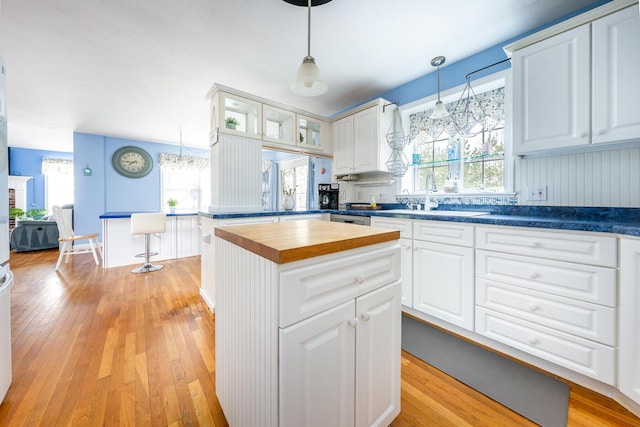 kitchen with wooden counters, a sink, light wood-style floors, white cabinetry, and a center island