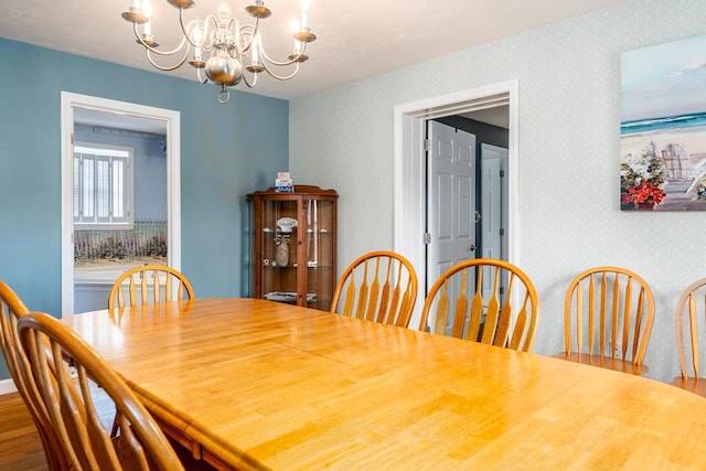 dining space with wallpapered walls, an inviting chandelier, and wood finished floors