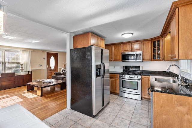 kitchen with light tile patterned flooring, stainless steel appliances, a sink, brown cabinets, and glass insert cabinets