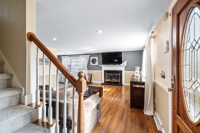 foyer with recessed lighting, baseboard heating, a glass covered fireplace, hardwood / wood-style floors, and stairs