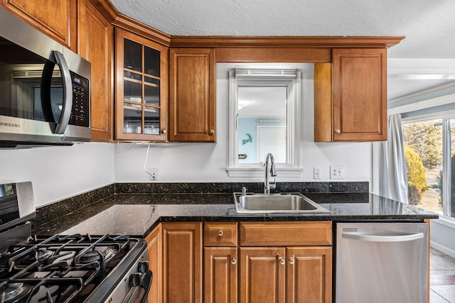 kitchen with stainless steel appliances, brown cabinetry, glass insert cabinets, a sink, and a textured ceiling