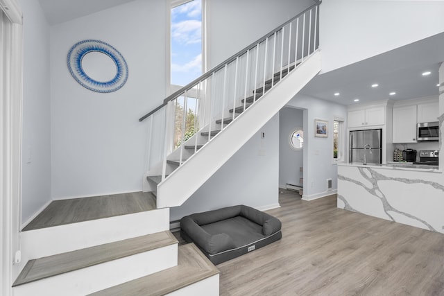 stairs with recessed lighting, baseboards, a high ceiling, visible vents, and wood finished floors