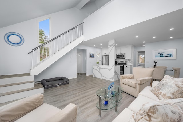 living room with a high ceiling, light wood-style flooring, stairway, and a baseboard radiator
