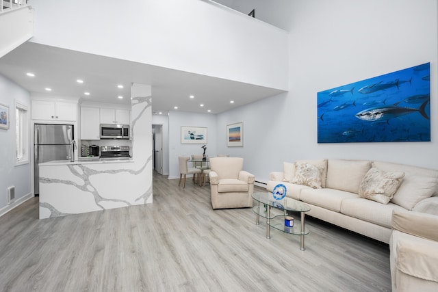 living area with a high ceiling, a baseboard radiator, light wood-style flooring, visible vents, and recessed lighting