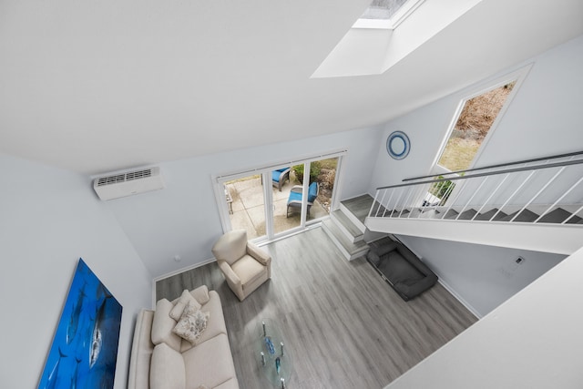 living room featuring a wall mounted AC, vaulted ceiling with skylight, baseboards, and wood finished floors