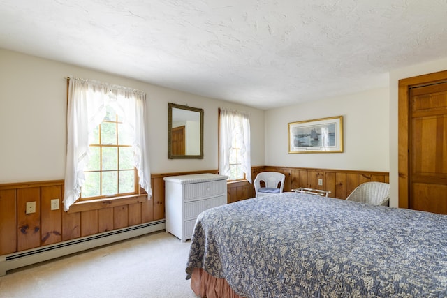 bedroom featuring wood walls, light colored carpet, a baseboard radiator, and a textured ceiling