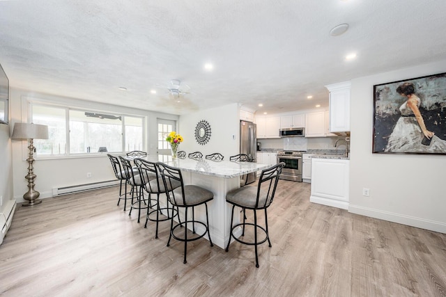 kitchen featuring a baseboard heating unit, a kitchen bar, light stone counters, white cabinets, and stainless steel appliances