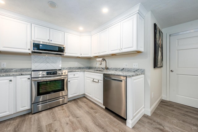 kitchen featuring light wood finished floors, white cabinetry, stainless steel appliances, and a sink