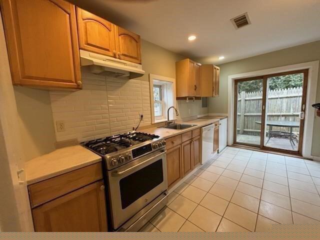 kitchen featuring dishwasher, sink, backsplash, light tile patterned floors, and stainless steel range with gas stovetop