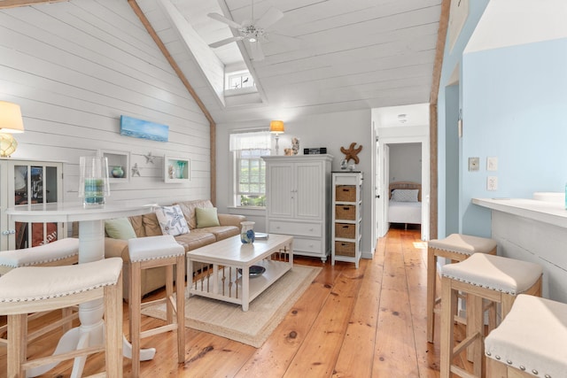 living room featuring ceiling fan, high vaulted ceiling, light wood-type flooring, and a skylight