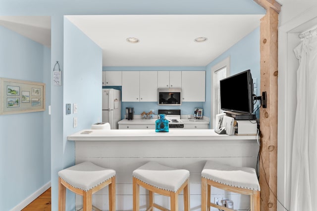 kitchen featuring white refrigerator, range with electric stovetop, white cabinets, and a breakfast bar