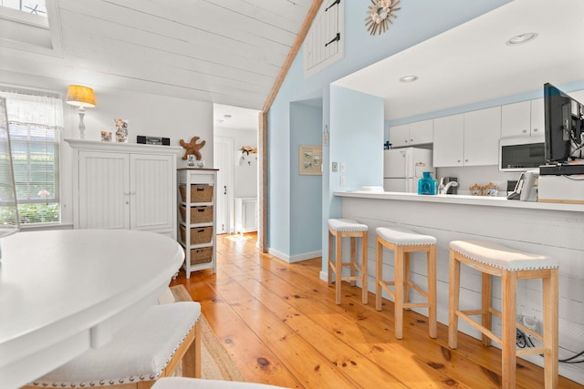 kitchen with lofted ceiling, light hardwood / wood-style floors, white cabinets, kitchen peninsula, and white fridge