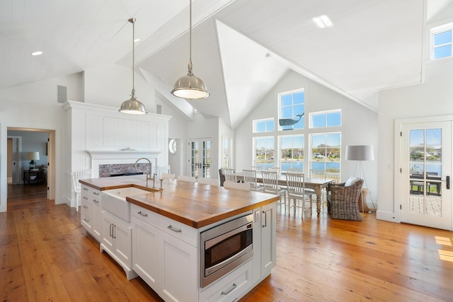 23 Oyster Pond Ln, Chatham, MA 02633 - kitchen with butcher block countertops, stainless steel microwave, white cabinets, a fireplace, and high vaulted ceiling