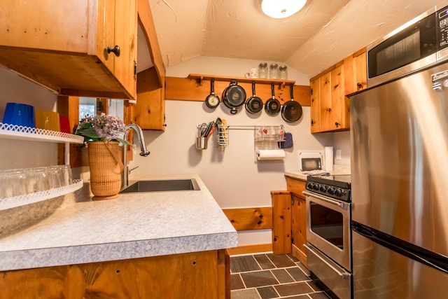 kitchen featuring light countertops, appliances with stainless steel finishes, brown cabinetry, and a sink