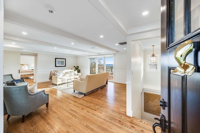 living area with a wainscoted wall, beam ceiling, light wood-type flooring, a decorative wall, and ornamental molding