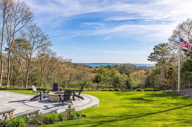 view of community with an outdoor fire pit, a patio, a forest view, and a lawn